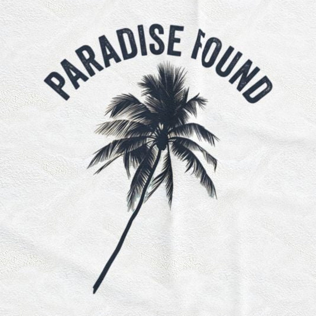Close-up of the Paradise Found print: a single dark palm silhouette under arched lettering, on the white velveteen throw